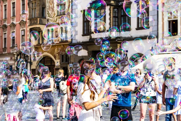 Menschen spielen mit Seifenblasen auf einem Platz in Prag, umgeben von historischen Gebäuden.