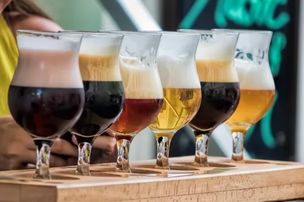 Sechs Gläser mit verschiedenen Biersorten in einer Holzhalterung, von dunkel bis hell.