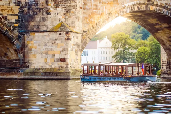 Ausflugsboot fährt auf der Moldau vor historischen Gebäuden und einem Turm.