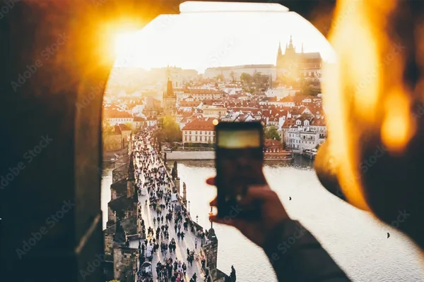 Blick durch einen Torbogen auf die Karlsbrücke in Prag bei Sonnenuntergang, mit Menschen und der Prager Burg im Hintergrund.