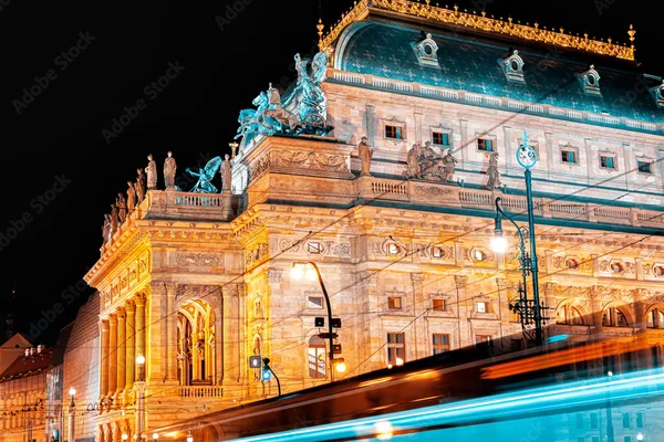 Beleuchtetes Nationaltheater in Prag mit vorbeifahrender Straßenbahn im Vordergrund.