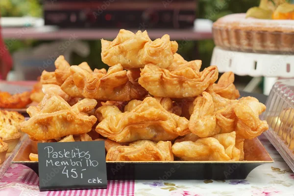 Tablett mit goldbraunen Teigtaschen und Preisschild auf einem Marktstand.