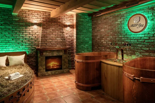 Rustikaler Wellnessraum mit Holzbadewannen, Zapfhähnen und Kamin.