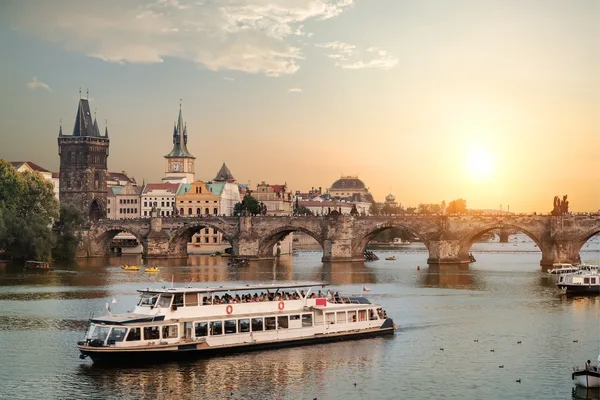 Ausflugsboot fährt bei Sonnenuntergang vor der Karlsbrücke und historischen Gebäuden in Prag.