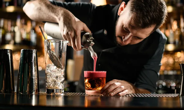 Bartender bereitet einen Cocktail an einer stilvollen Bar mit glänzenden Shakern und Gläsern.