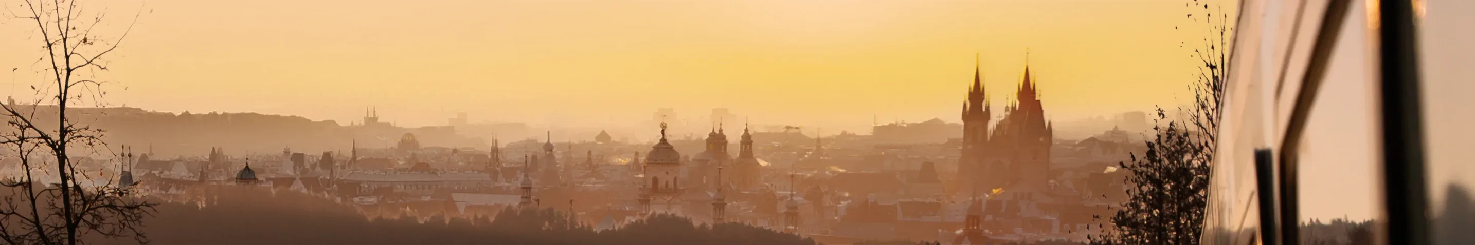 Blick auf die Silhouette von Prag bei Sonnenaufgang. Die historischen Türme und Dächer der tschechischen Hauptstadt leuchten im warmen Morgenlicht, während rechts ein alex-Zug ins Bild ragt.