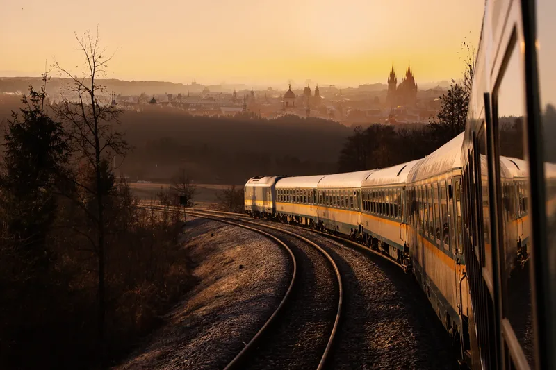 Ein alex-Zug schlängelt sich auf den letzten Kilometern vor Prag durch die winterliche Landschaft. Die goldene Morgensonne taucht die Dächer und Türme der Stadt in warmes Licht.