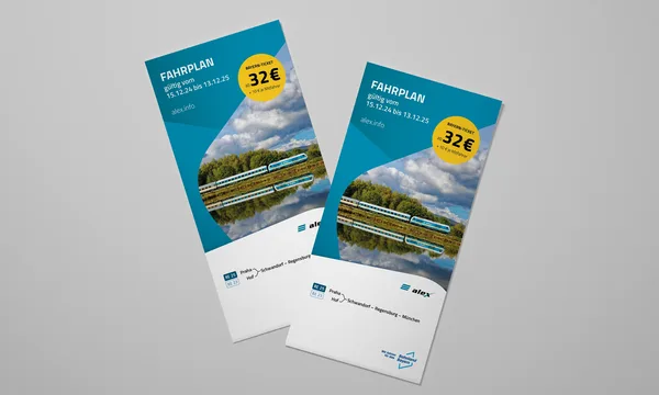 Dva letáky s názvem „FAHRPLAN“ leží na šedém povrchu. Oba zobrazují fotografii krajiny s řekou a stromy pod modrou oblohou s mraky. Na letácích je uvedeno „FAHRPLAN platný od 15.12.24 do 13.12.25“ spolu s webovou stránkou „alex.info“. Žlutý kruh zvýrazňuje cenu „32 € + 10 € za každého dalšího spolucestujícího“. Dole jsou loga „alex“ a „BEG“ a také trasa „Praha – Schwandorf – Řezno – Mnichov“.