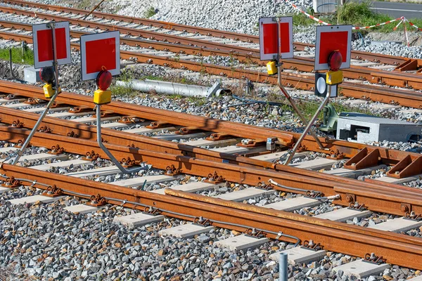 Mehrere Gleissperrsignale mit roten Tafeln und Signalleuchten stehen entlang von Bahngleisen auf einem Schotterbett.