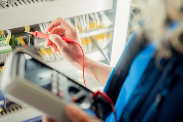 Hand hält Prüfgerät an Kabeln im Schaltschrank zur Kontrolle der Elektronik.