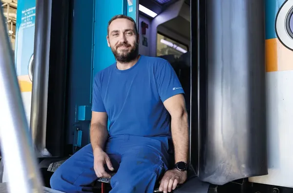 Person in blauer Arbeitskleidung sitzt am Einstieg eines alex-Zuges in der Werkstatt.
