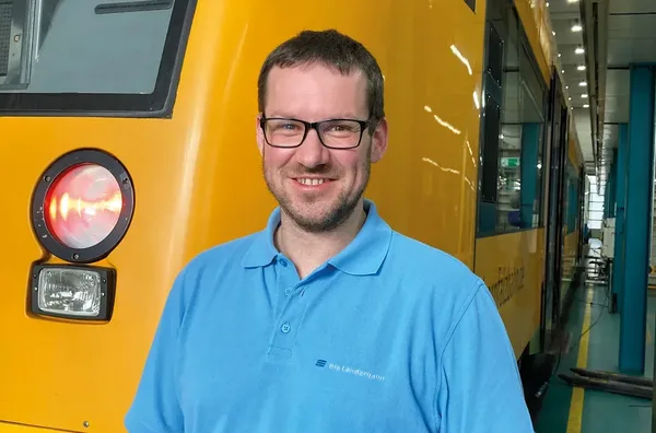Person in blauem Oberteil steht in der Werkstatt vor einem gelben oberpfalzbahn-Zug.