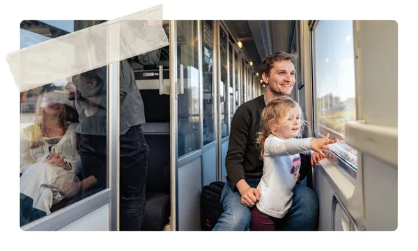 Ein Erwachsener sitzt mit einem Kind am Fenster im Zug. Das Kind zeigt nach draußen auf die vorbeiziehende Landschaft, während weitere Fahrgäste im Hintergrund zu sehen sind.