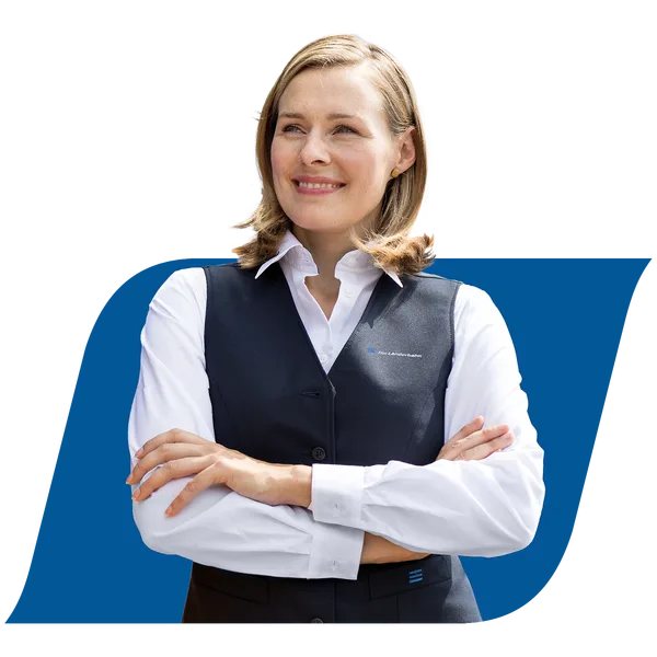 Obrázek zobrazuje zaměstnankyni společnosti Die Länderbahn GmbH DLB s překříženýma rukama. Stojí před neutrálním pozadím a s úsměvem se dívá do dálky.