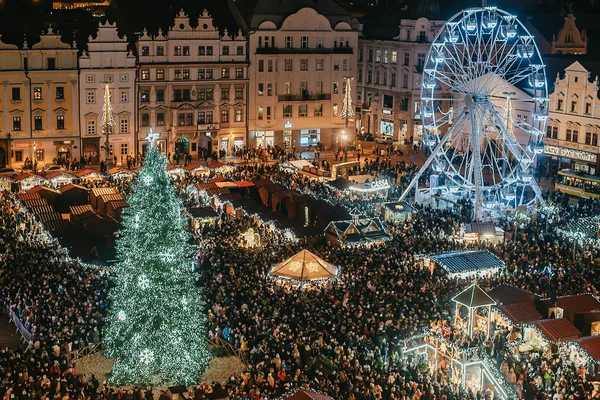 Großer Weihnachtsmarkt auf einem historischen Platz mit beleuchtetem Riesenrad, geschmücktem Weihnachtsbaum und dichtem Gedränge von Besuchern.