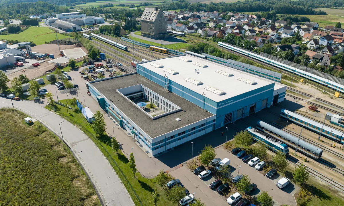 Luftaufnahme eines großen Werkgebäudes mit Gleisanlagen, Zügen und umliegender Landschaft in Schwandorf.