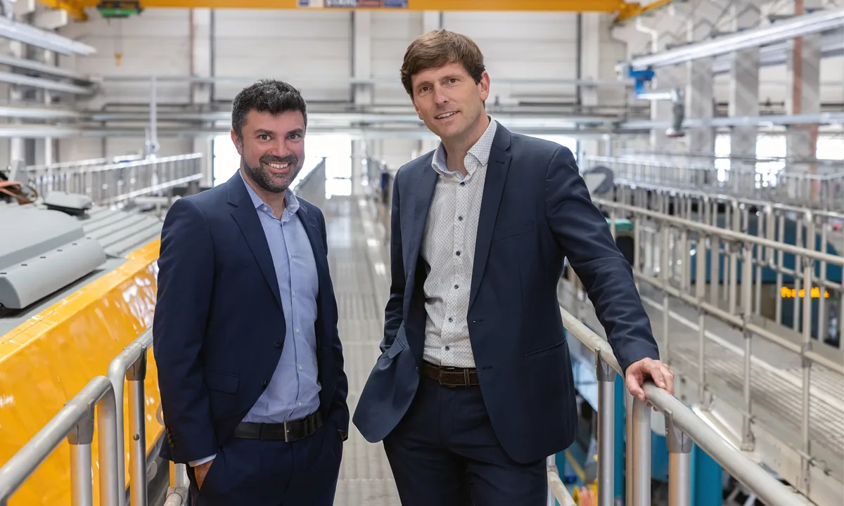 Die Geschäftsführer Eugen Rubinstein und Stefan Naue stehen freundlich lächelnd in der Werkhalle Schwandorf mit einem gelben Zug im Hintergrund.