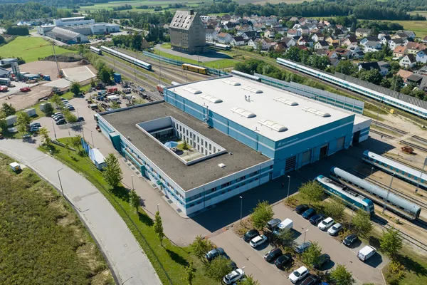 Luftaufnahme eines großen Werkgebäudes mit Gleisanlagen, Zügen und umliegender Landschaft in Schwandorf.
