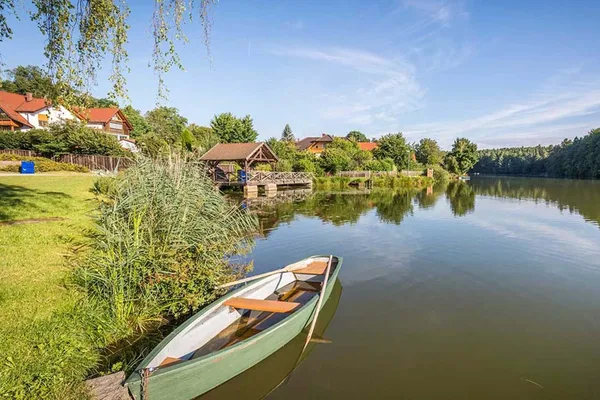 Grünes Ruderboot am Ufer eines Sees, welcher umgeben von Wald und einzelnen Häusern ist