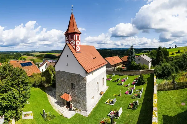 Auf dem Bild ist die Kirche St. Ulrich in Wilchenreuth zu sehen. Sie ist von oben fotografiert und man kann in den umliegenden Friedhof sehen.