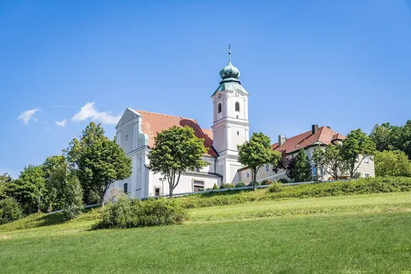 Das Bild zeigt die Klosterkirche St. Felix auf einem Hügel. Vor der Kirche sind ansteigende Wiesen und einzelne Bäume zu sehen.