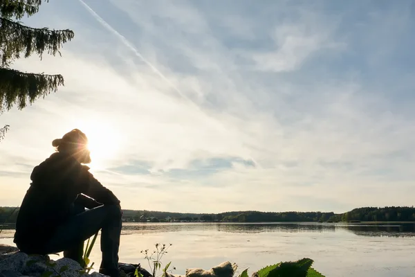 Ein Mann schaut im Sonnenuntergang auf einen See.