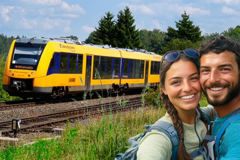 Zwei Personen vor einem gelben Zug der Länderbahn an einer Bahnstrecke im Grünen
