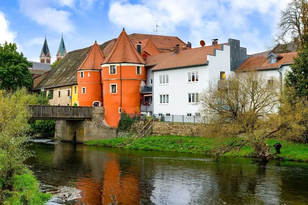 Historische Häuser mit Turm und roten Dächern an einem Flusslauf