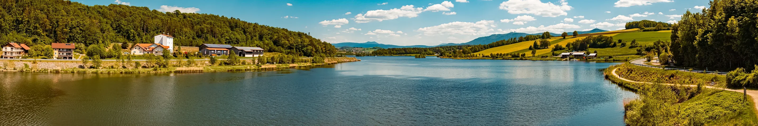 Blick auf einen breiten, ruhigen See. Er ist umgeben von Hügeln und Wäldern