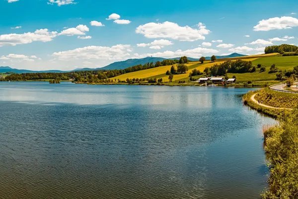 Blick auf einen breiten, ruhigen See. Er ist umgeben von Hügeln und Wäldern