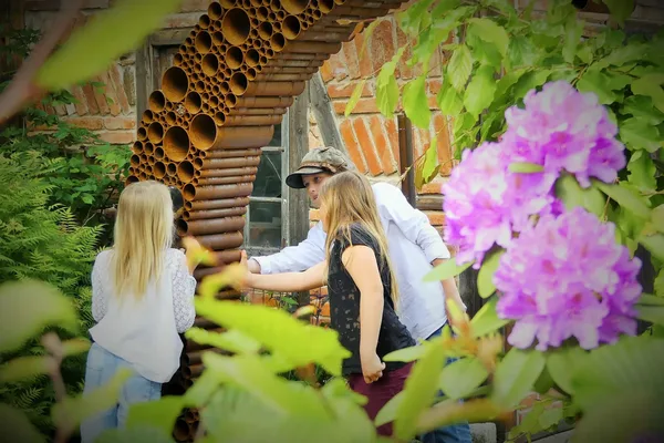 Personen stehen vor einem Torbogen aus Naturmaterialien in einem Garten