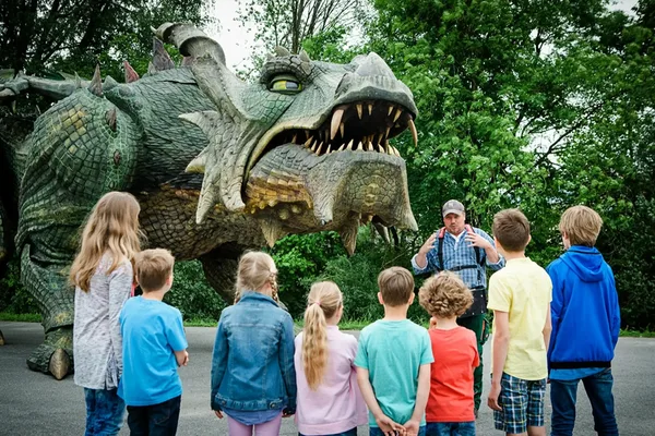 Kinder betrachten eine große grüne Drachenstatue in einer Parkanlage