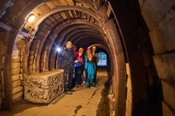 Gruppe von Personen mit Helmen und Lampen in einem gemauerten unterirdischen Stollen