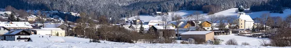 Verschneite Dorflandschaft mit Schnee auf Dächern und Wiesen