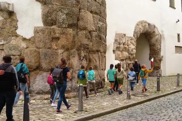Besuchergruppe aus Kindern und Erwachsenen passiert ein altes Steintor in einer Altstadt