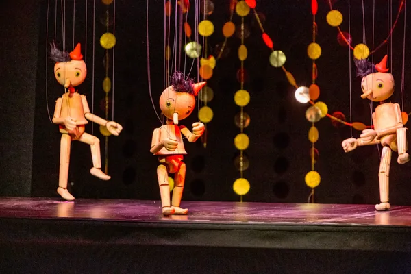 Mehrere hölzerne Marionetten stehen auf einer beleuchteten Bühne