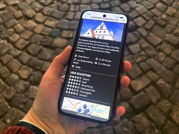 Eine Hand hält ein Smartphone. Darauf ist die App Actionbound mit der Stadtrallye in Weiden zu sehen.