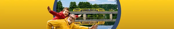 Ein älterer Mann in gelber Regenjacke trägt einen Jungen mit roter Regenjacke Huckepack. Im Hintergrund fährt die oberpfalzbahn an einem Fluss entlang, in dem sie sich spiegelt.
