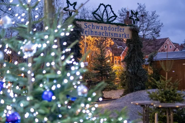 Blick auf den Eingang des Schwandorfer Weihnachtsmarkts. Im Vordergrund ist unscharf eine Tanne mit Lichterkette zu erkennen.
