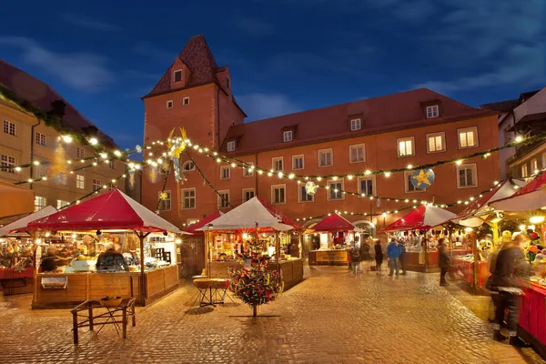 Verschiedene Weihnachtsmarktbuden in Abendstimmung mit Lichterketten am Regensburger Haidplatz.