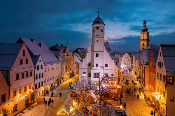 Blick auf den Christkindlmarkt in Weiden. Buden und Hausfassaden sind beleuchtet. Im Zentrum des Bildes ist die Kirche mit Kirchturm zu sehen,.