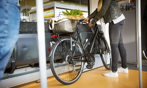 Fahrrad steht im Innenraum eines Zuges, beladen mit Einkaufstasche und Blumen im Korb.