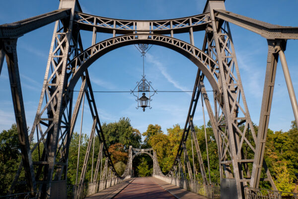 Historische Stahlbrücke auf der Peißnitzinsel in Halle (Saale), umgeben von Bäumen und Grünflächen.