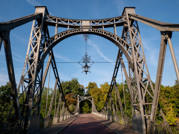 Historische Stahlbrücke auf der Peißnitzinsel in Halle (Saale), umgeben von Bäumen und Grünflächen.