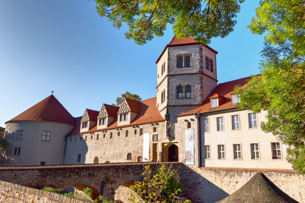 Historische Moritzburg in Halle (Saale) mit ihren hellen Natursteinmauern, roten Dächern und markanten Türmen. Die ehemalige Burganlage, heute Kunstmuseum, ist von Bäumen umgeben und zählt zu den bedeutendsten Sehenswürdigkeiten der Stadt.