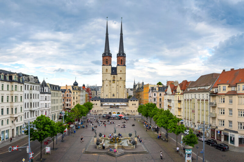 Panoramablick über den Marktplatz in Halle (Saale) mit dem Roten Turm und den markanten Türmen der Marktkirche Unser Lieben Frauen. Umgeben von historischen Gebäuden, Geschäften und Cafés bildet der Platz das lebendige Zentrum der Altstadt.