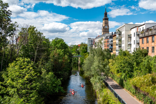 Kanufahrer auf einem Kanal in Leipzig zwischen grünen Ufern und städtischer Bebauung.