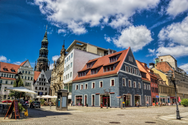 Historischer Hauptmarkt in der Zwickauer Altstadt mit farbenfrohen Bürgerhäusern, Cafés und dem Dom St. Marien im Hintergrund unter blauem Himmel mit weißen Wolken