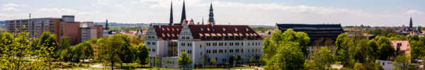 Historisches Gebäude in Zwickau mit heller Fassade und roten Ziegeldächern, umgeben von Grünflächen und Bäumen: August-Horch Museum. Im Hintergrund prägen mehrere Kirchtürme die Stadtsilhouette, während im Vordergrund Straßen und Wege durch eine parkähnliche Umgebung führen.