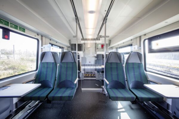 Das Bild zeigt den Innenraum eines Siemens Mireo-Zugs. Zu sehen sind mehrere Sitze, Tische sowie die Tür, die den Übergang zur 1. Klasse bildet.